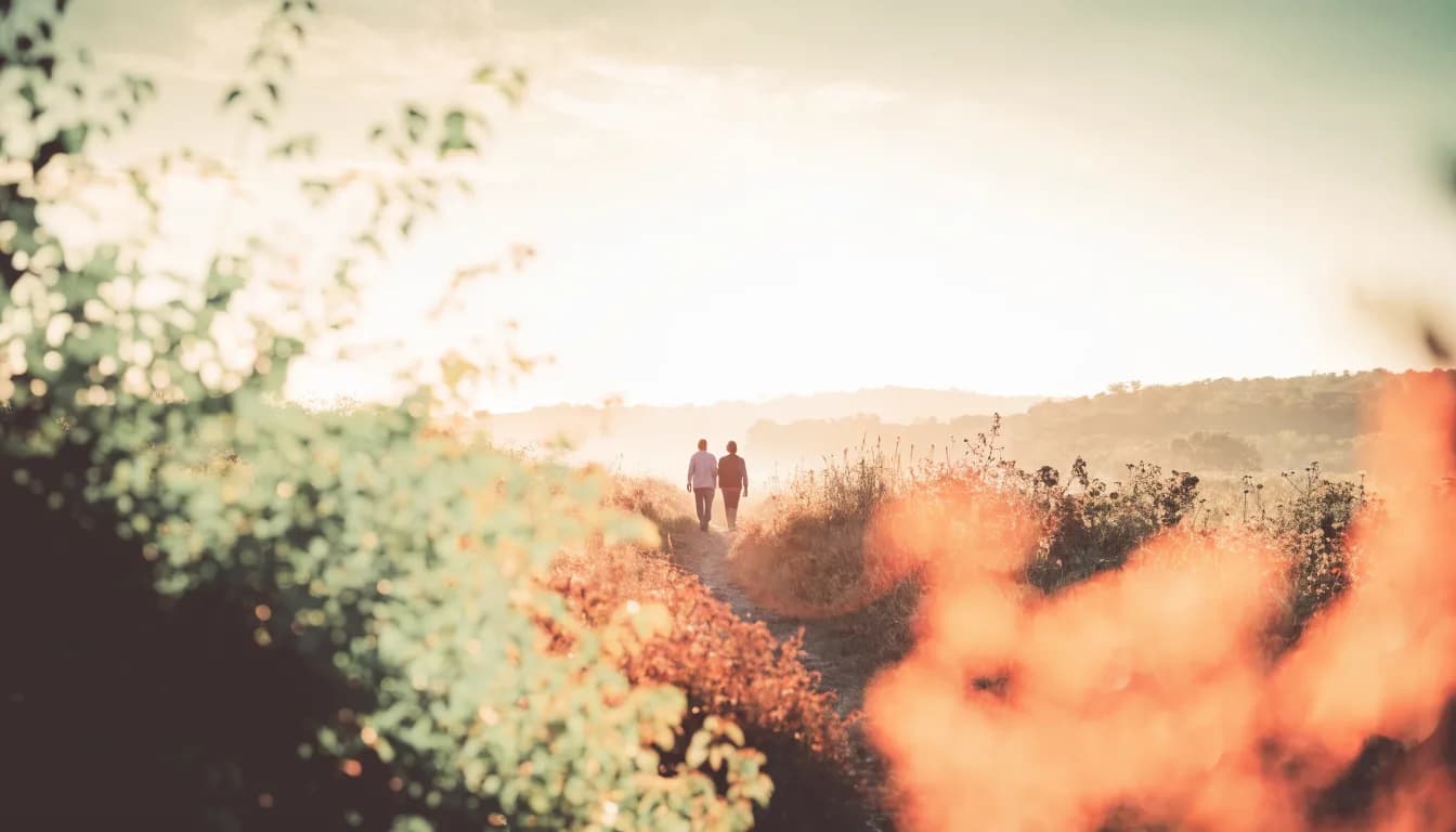 A couple walks together along a quiet path at sunrise, seen softly from behind, suggesting hope and a shared journey of healing.