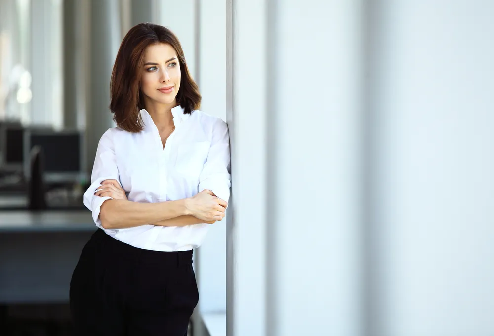 A woman standing calmly by a bright window, arms folded, with a steady expression