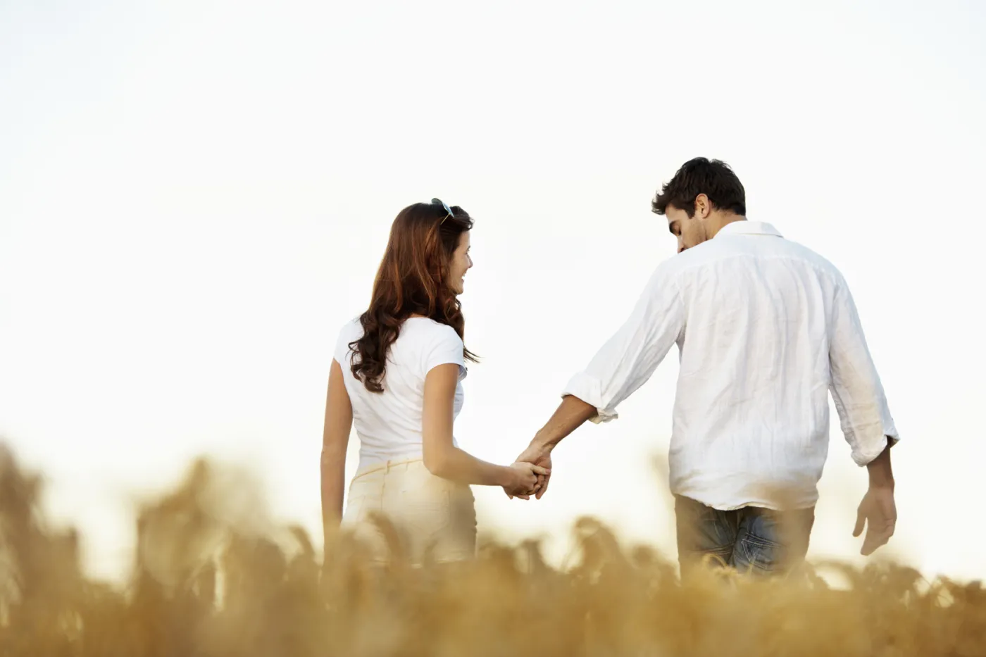 A couple holding hands, walking together through a field at sunset
