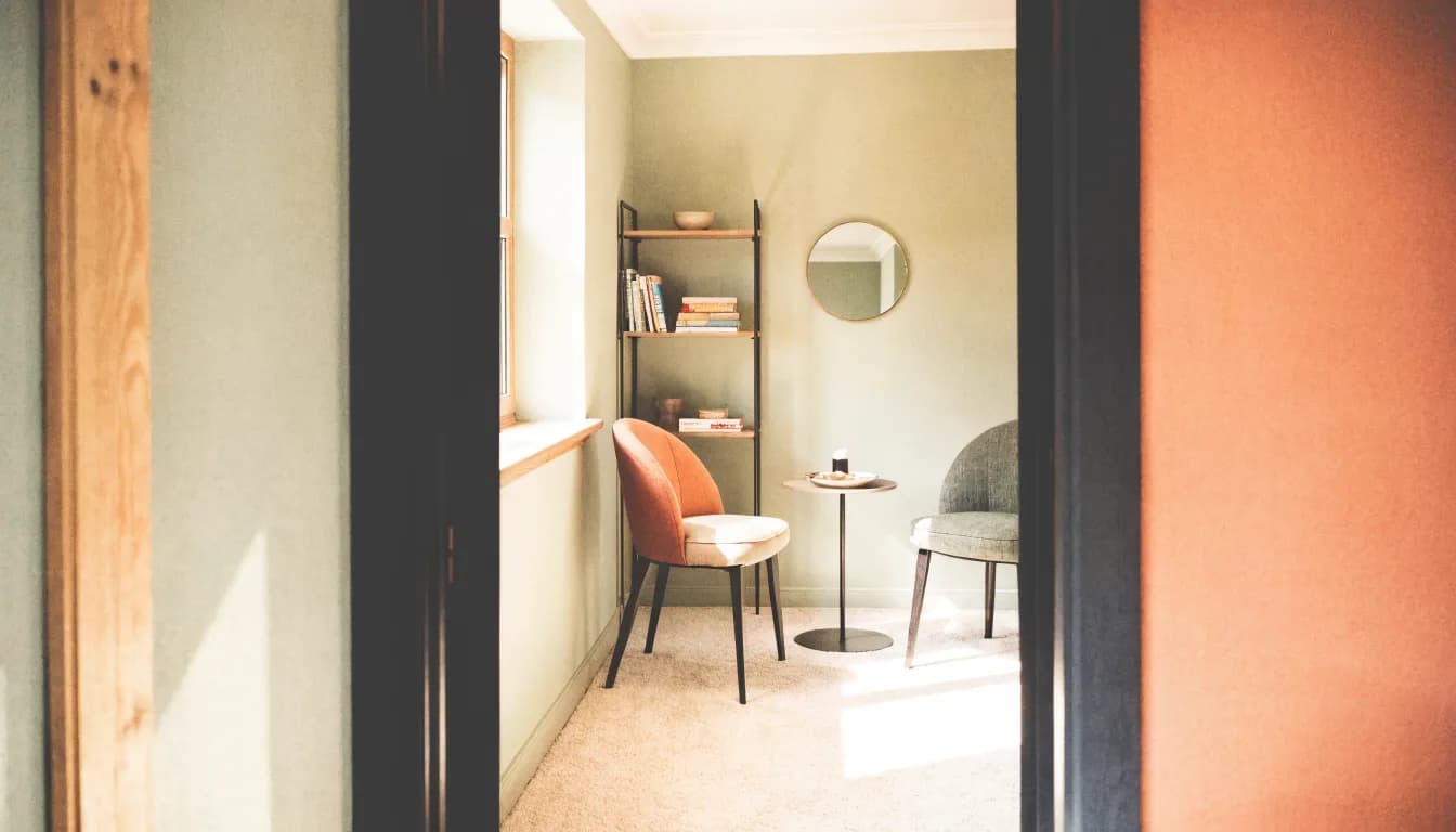 A welcoming counseling-office doorway with warm light spilling onto two comfortable chairs arranged just inside, ready for a first session.