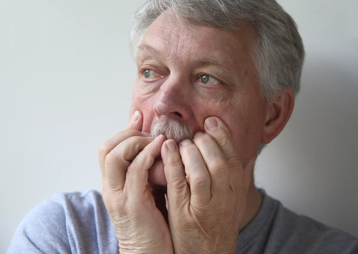 An older man sitting alone, looking worried