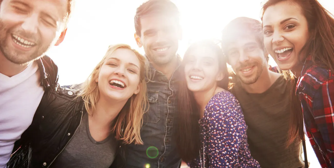 A group of friends laughing together outdoors in warm sunlight