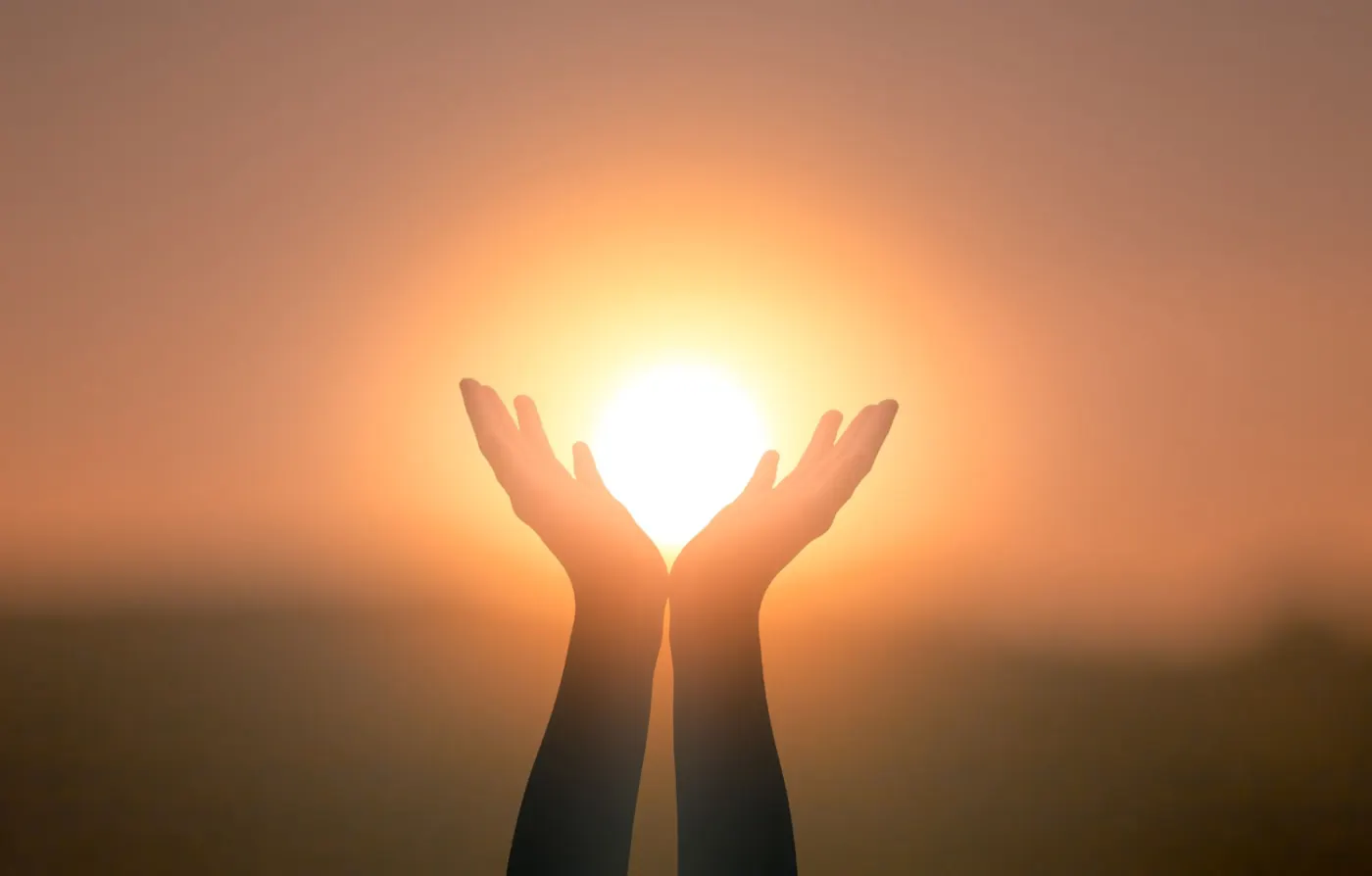 Open hands held up around a glowing sunset