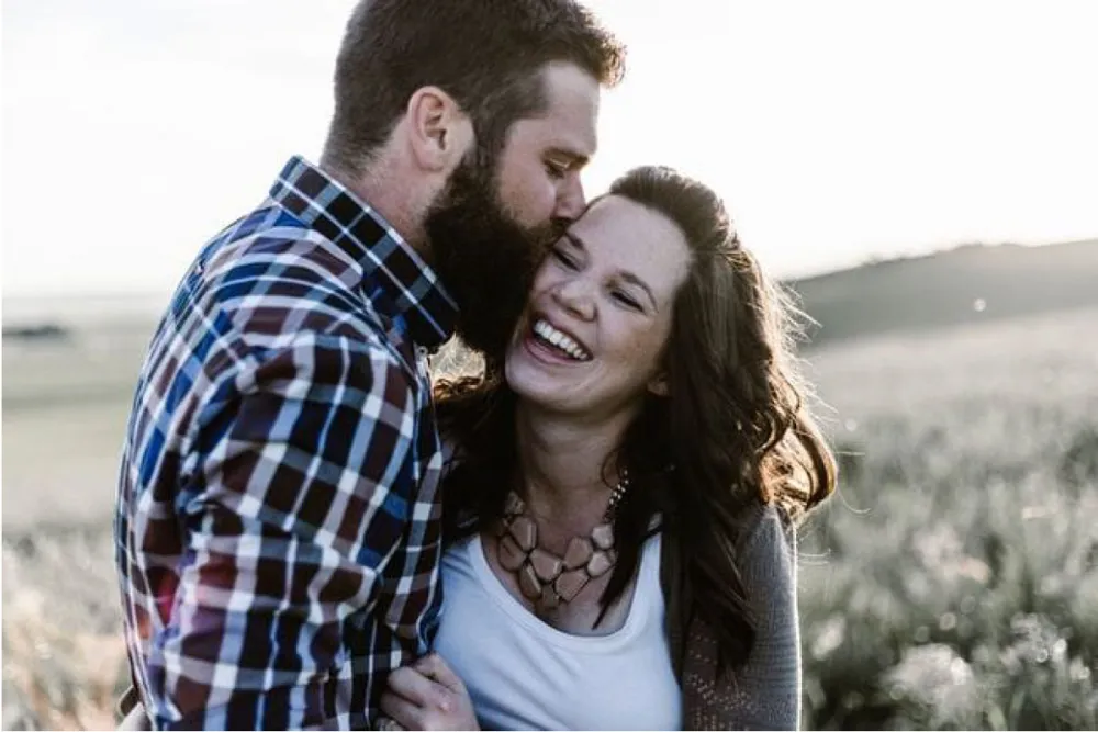 A couple laughing together outdoors as he kisses her cheek