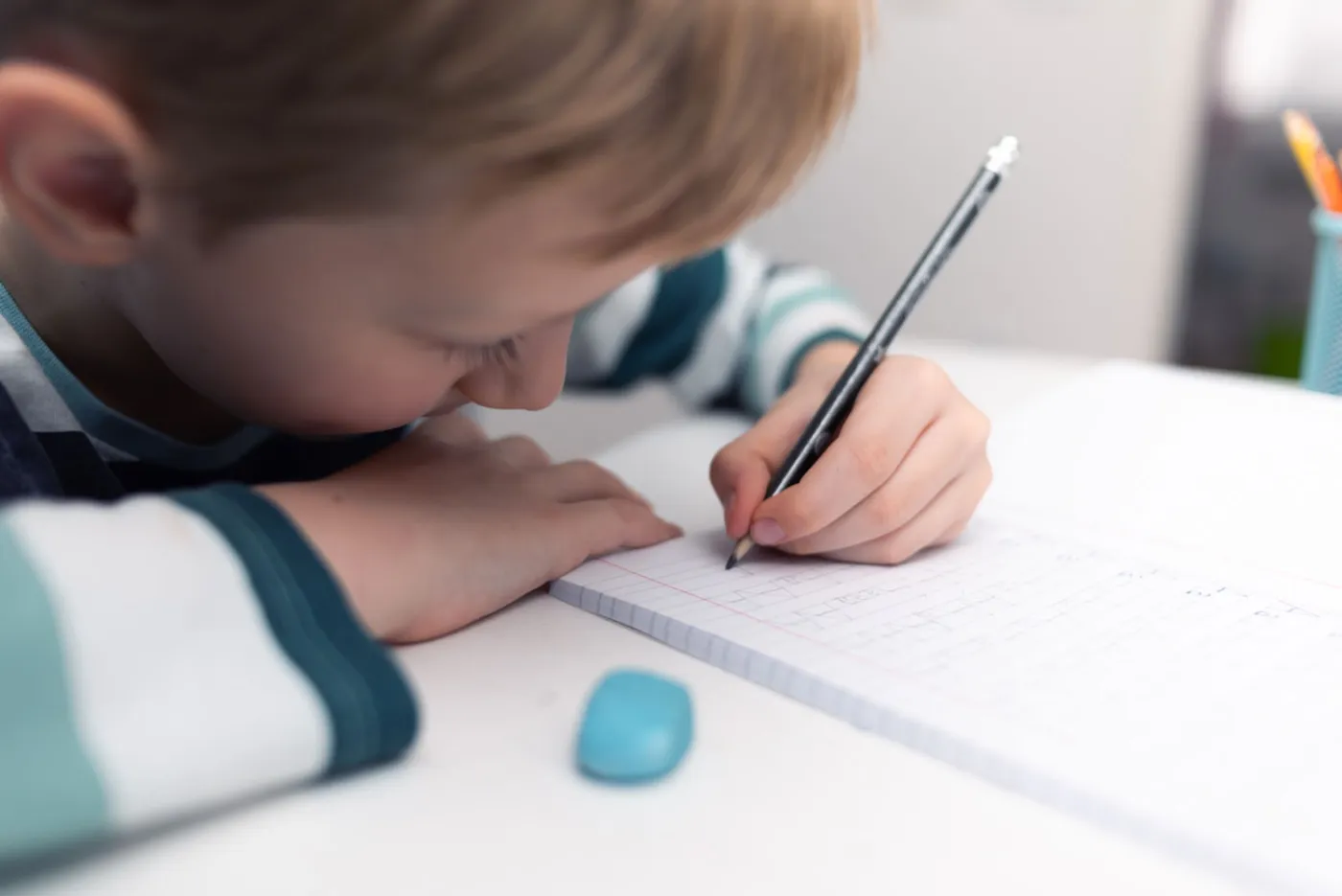 A young child concentrating while writing on graph paper at a desk